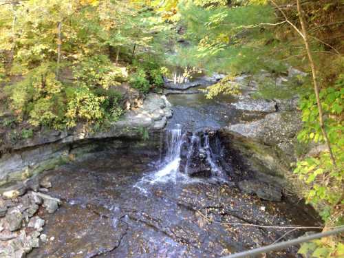 A serene waterfall cascades over rocky terrain, surrounded by vibrant autumn foliage.