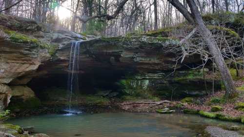 A serene waterfall cascades into a tranquil pool, surrounded by mossy rocks and trees in a peaceful forest setting.