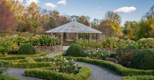 A serene garden with a stone gazebo surrounded by lush greenery and colorful autumn foliage.