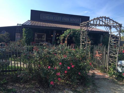 A rustic winery building surrounded by a garden with roses and a wooden archway, under a clear blue sky.
