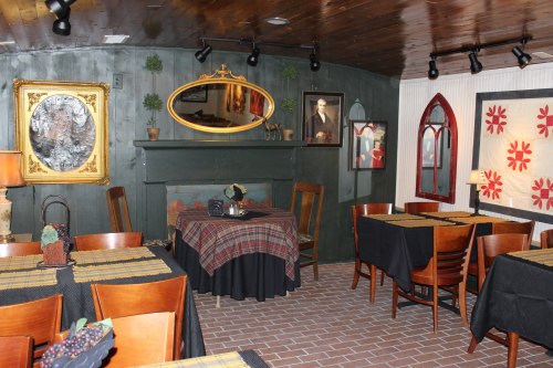 Cozy restaurant interior with dark wood accents, tables set with black linens, and decorative artwork on the walls.