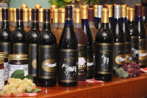 A display of various wine bottles with unique labels, alongside jars and fresh grapes on a wooden table.
