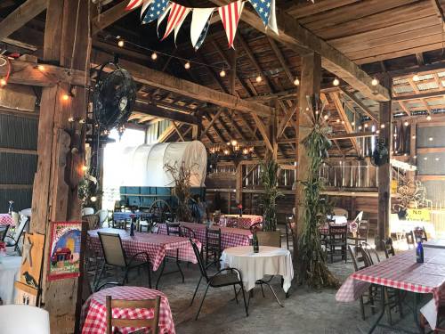 Interior of a rustic barn restaurant with checkered tablecloths, string lights, and vintage decor.