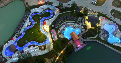 Aerial view of a resort with multiple pools, lounge chairs, and landscaped areas near a body of water.
