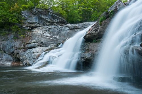 A serene waterfall cascading over rocky cliffs into a calm pool, surrounded by lush green trees.