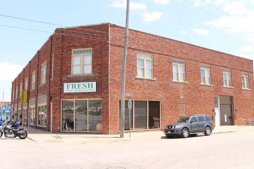 A brick building with large windows, featuring a sign that reads "FRESH," located on a street corner.