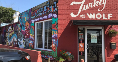 Colorful mural on a brick building with the sign "Turkey and the Wolf" and vibrant flowers in front.