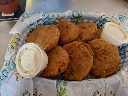 A basket of golden-brown fried green tomatoes with two dipping sauces on the side, served in a colorful paper liner.