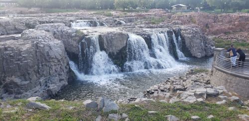 A scenic view of a waterfall cascading over rocky cliffs, with a person standing by a railing nearby.
