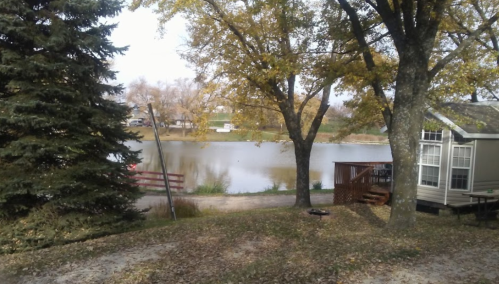 A serene lakeside view with autumn trees, a small cabin, and a calm water surface reflecting the surroundings.