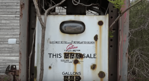 An old, rusty gas pump with a faded sign reading "THIS FOR SALE" and a note about glass being full before delivery.