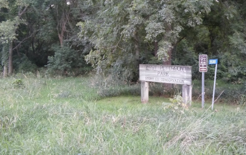 Sign for West Peterson Park in Story County Conservation, surrounded by trees and tall grass.