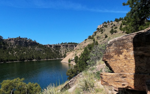 A serene lake surrounded by rocky cliffs and green trees under a clear blue sky.