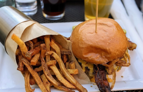 A juicy burger with bacon and cheese, served with a side of crispy fries in a paper cone.