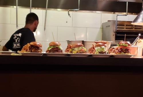A chef prepares burgers with toppings and fries in a restaurant kitchen.