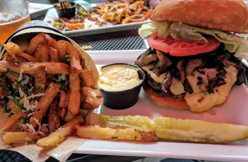 A hearty burger with lettuce, tomato, and cheese, served with crispy fries and a side of dipping sauce and a pickle.