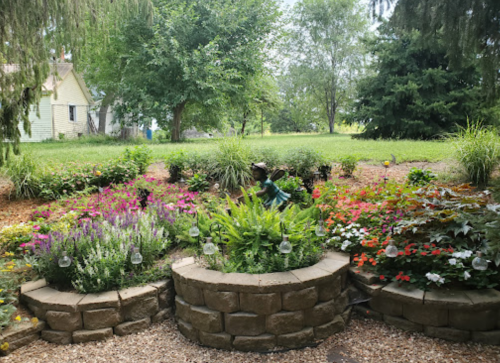 A lush garden with colorful flowers and greenery, featuring a child tending to the plants in the background.