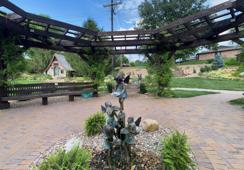 A garden scene featuring a decorative wooden arch, a stone pathway, and a bronze statue of children playing.