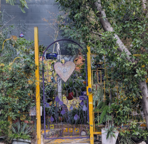A colorful garden gate adorned with a heart, surrounded by lush greenery and vibrant plants.