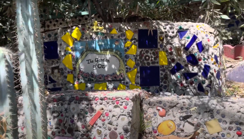 Colorful mosaic wall with the text "The Garden of Oz," surrounded by greenery and decorative tiles.