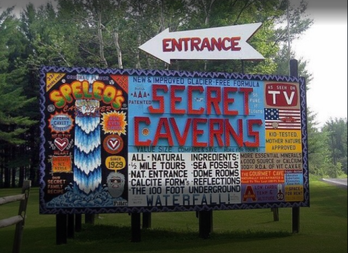 Colorful sign for Secret Caverns, featuring attractions, ingredients, and directions, surrounded by trees.