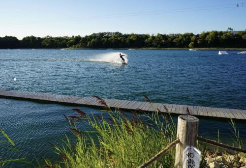 A person water skiing on a calm lake, with a wooden dock and lush greenery in the background.