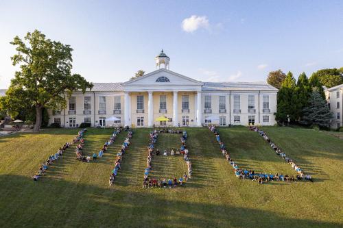 Aerial view of a large group of people forming the letters "NBL" on a grassy hill in front of a historic building.