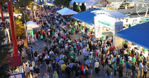 Aerial view of a crowded outdoor event with people in green attire, food stalls, and festive lights.