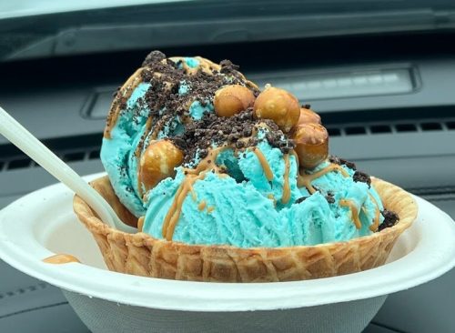 A bowl of blue ice cream topped with crushed cookies and caramel, sitting in a car.