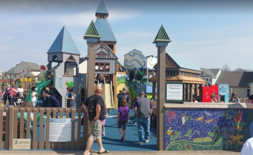 A colorful playground with various structures and children playing, surrounded by families enjoying the day.