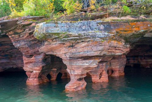 Rock formations with unique pillars rise from clear water, surrounded by lush greenery and autumn foliage.