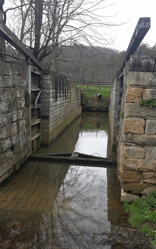 A stone lock structure with water reflecting the surrounding trees and hills, creating a serene landscape.