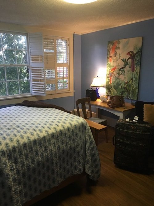 Cozy bedroom with a blue wall, a bed with a quilt, a desk, a lamp, and a suitcase in the corner.