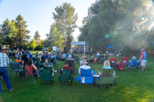 A crowd of people sitting in lawn chairs at an outdoor event, enjoying a performance under a clear blue sky.