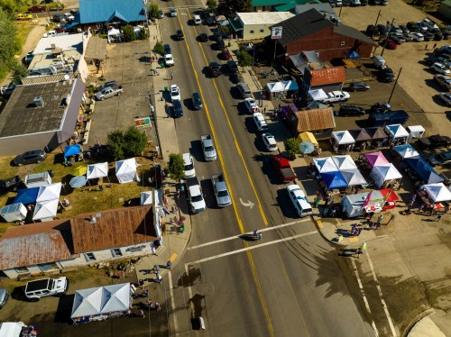 Aerial view of a street lined with tents, parked cars, and people, showcasing a vibrant outdoor market scene.