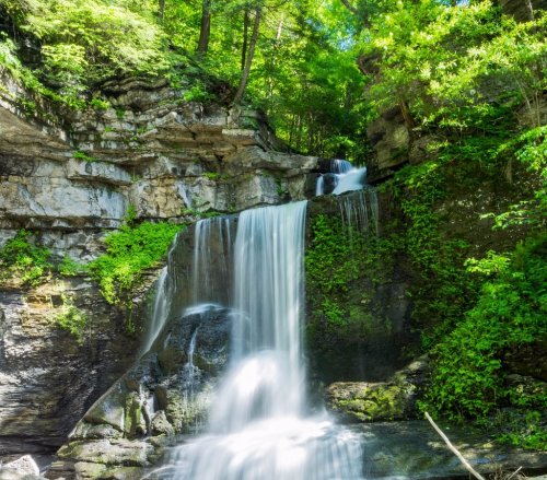 A serene waterfall cascading over rocky cliffs, surrounded by lush green foliage and trees.