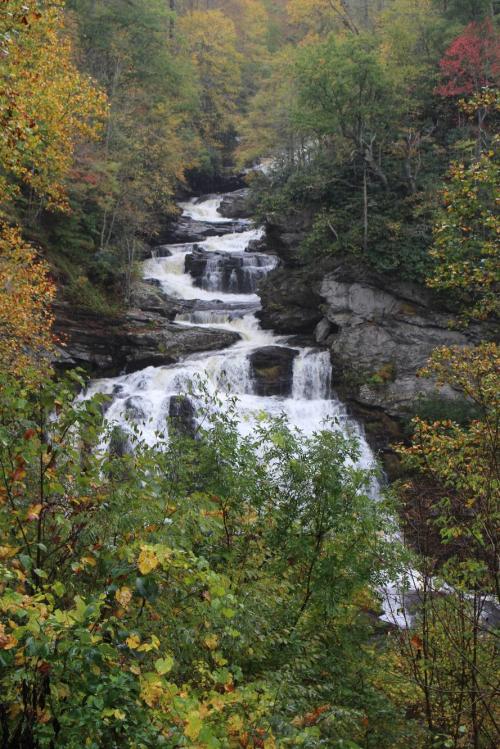 A cascading waterfall surrounded by vibrant autumn foliage and rocky terrain.