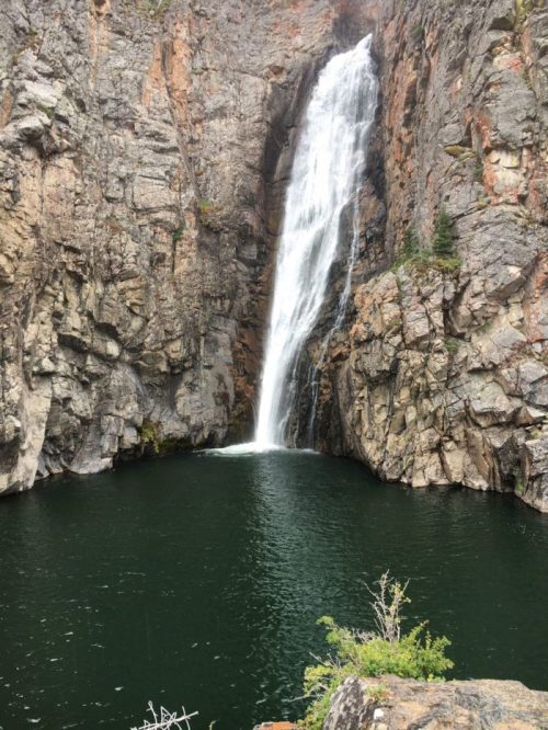A stunning waterfall cascades down rocky cliffs into a serene, dark green pool below.