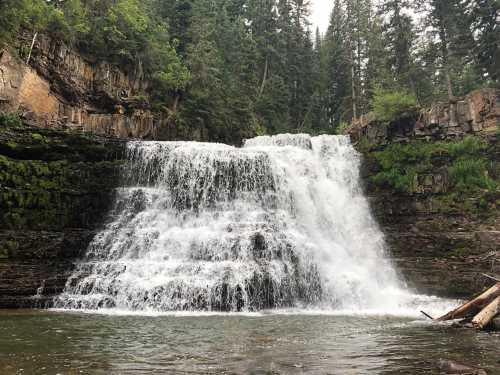 A cascading waterfall surrounded by lush green trees and rocky cliffs, creating a serene natural scene.