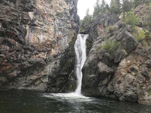 A waterfall cascading down rocky cliffs into a serene green pool surrounded by trees.