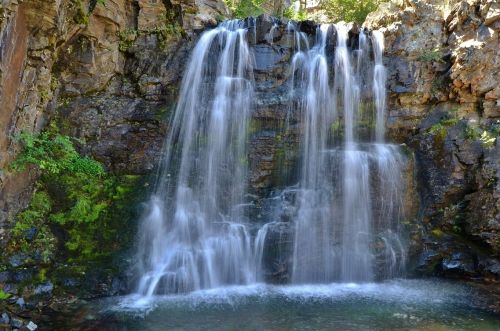 A serene waterfall cascading over rocky cliffs into a clear pool, surrounded by lush greenery.