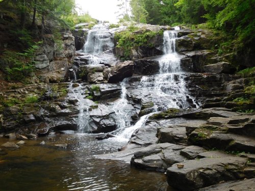 A serene waterfall cascading over rocky terrain, surrounded by lush greenery and a calm pool at the base.
