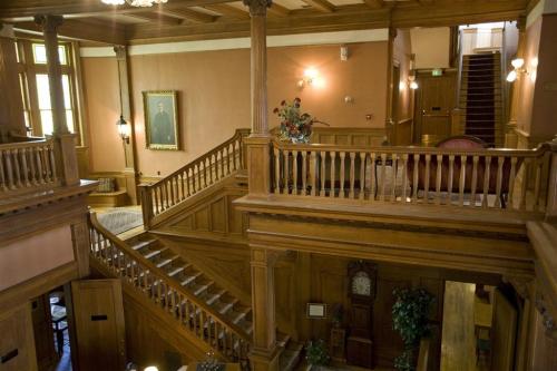 A spacious wooden interior with a staircase, ornate railings, and a portrait on the wall, showcasing classic architecture.