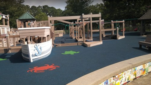 A colorful playground featuring a boat structure, climbing equipment, and rubber flooring with sea creature designs.
