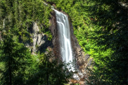 A cascading waterfall surrounded by lush green trees and rocky cliffs in a serene natural setting.