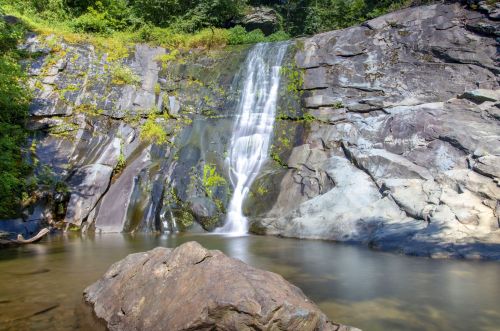 A serene waterfall cascading over rocky cliffs into a calm pool, surrounded by lush greenery.