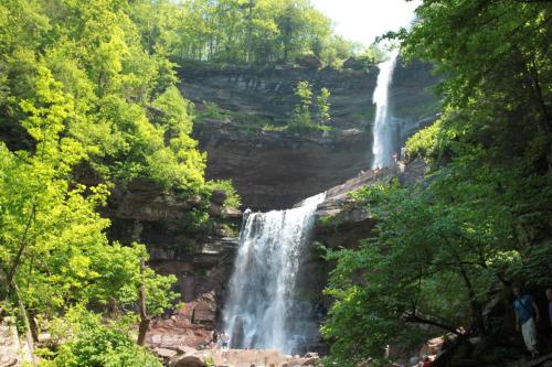 A scenic view of a waterfall cascading down rocky cliffs, surrounded by lush green trees and visitors enjoying the area.