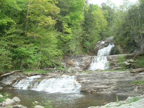 A serene waterfall cascades over rocky terrain, surrounded by lush green trees and foliage.