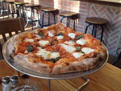 A freshly baked pizza on a metal stand, topped with mozzarella, basil, and marinara sauce, in a cozy restaurant setting.