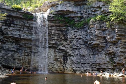A scenic waterfall cascades into a natural pool, surrounded by rocky cliffs and people enjoying the water.